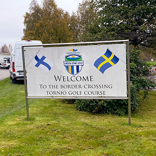 Skylt med texten Welcome to the border-crossing Tornio golf course, svensk och finsk flagga och golfklubbens emblem.